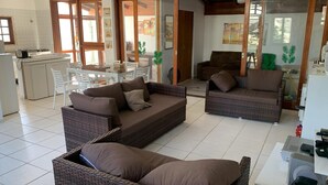 A spacious living area with wicker furniture, a dining table, and a kitchen in the background. - 4 suites WITH AIR CONDITIONING + 1 bedroom-living room with bathroom 2 refrigerators barbecue garden terrace TV DVD YT (São Sebastião)