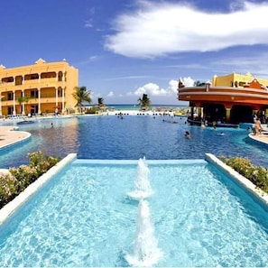 Relax by the resort's central pool, surrounded by lush palm trees and a picturesque landscape.