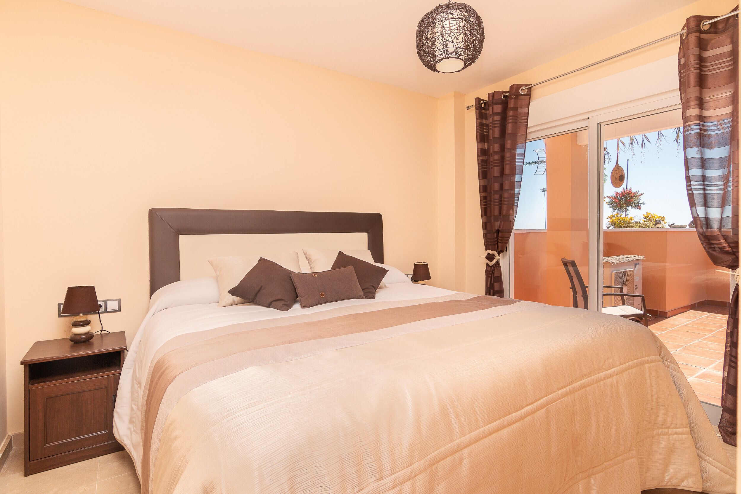 A bedroom with a bed, nightstand, lamp, and a view of the outside balcony.