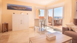 A modern living room with a glass door leading to a balcony, a dining area, and a large painting on the wall.