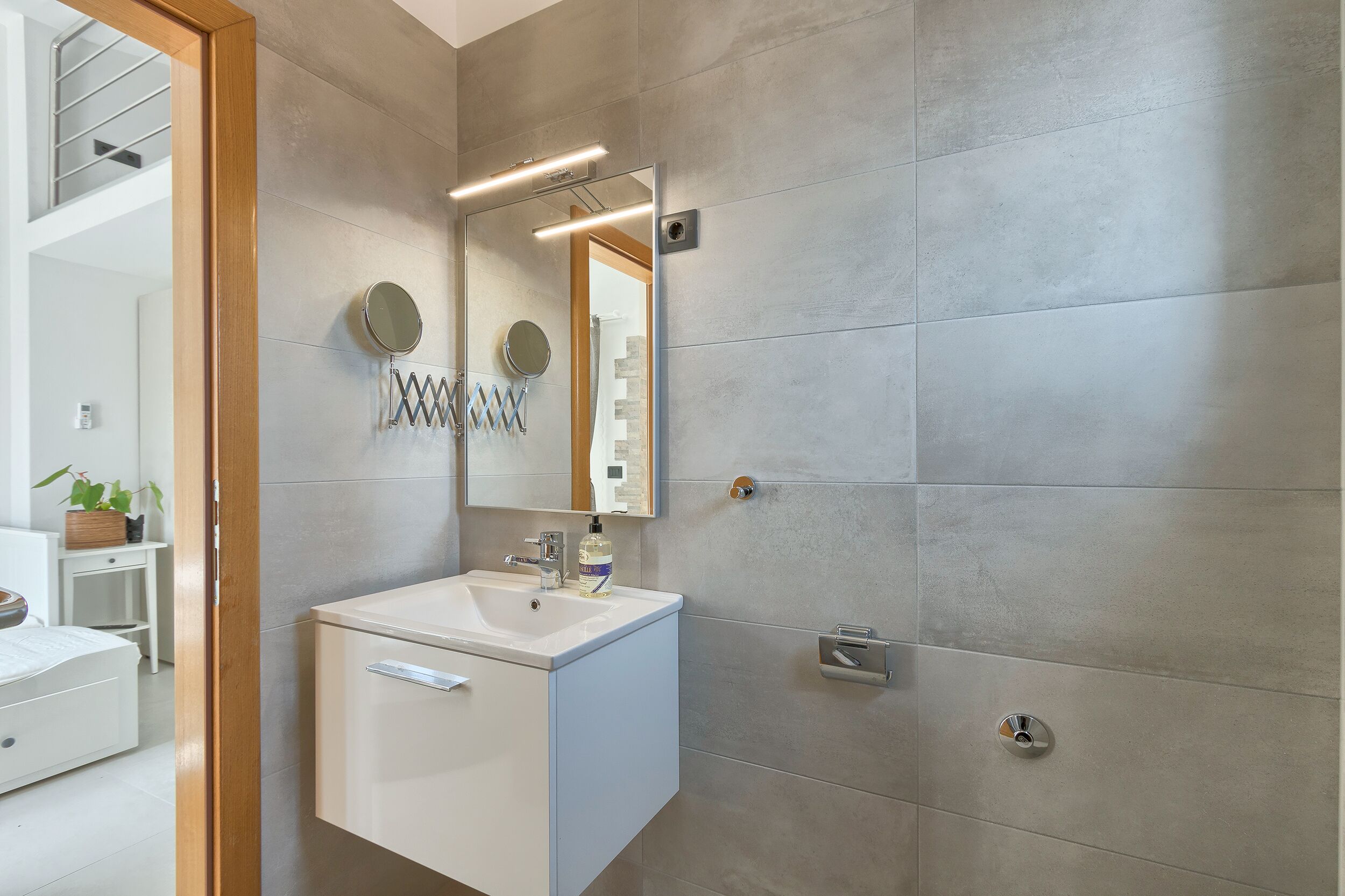 Un baño moderno con un lavamanos blanco, un espejo y un perchero para toallas.