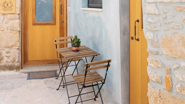 A stone building with a wooden door and a small table with chairs. - Evans House II One Bedroom Maisonette (Chania)
