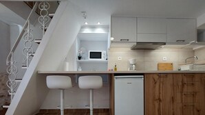 A compact kitchen with a dishwasher, a microwave, and a coffee maker. There are two white bar stools and a wooden cabinet. - Evans House II One Bedroom Maisonette (Chania)