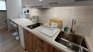 A modern kitchen with a built-in stove, a sink, and wooden cabinets. - Evans House II One Bedroom Maisonette (Chania)