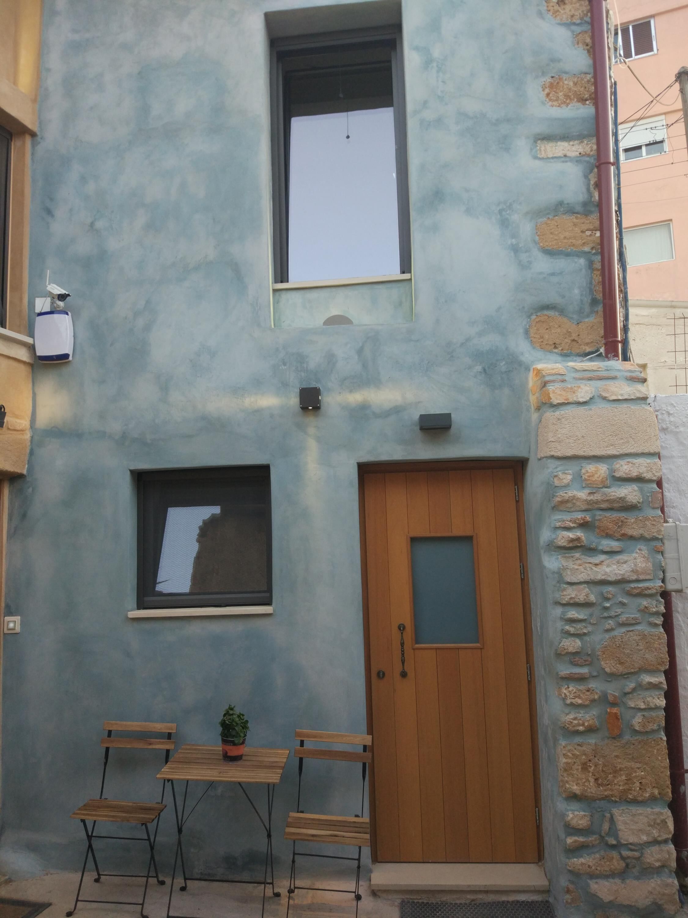 A two-story building with a blue facade, a wooden door, and a small window.
