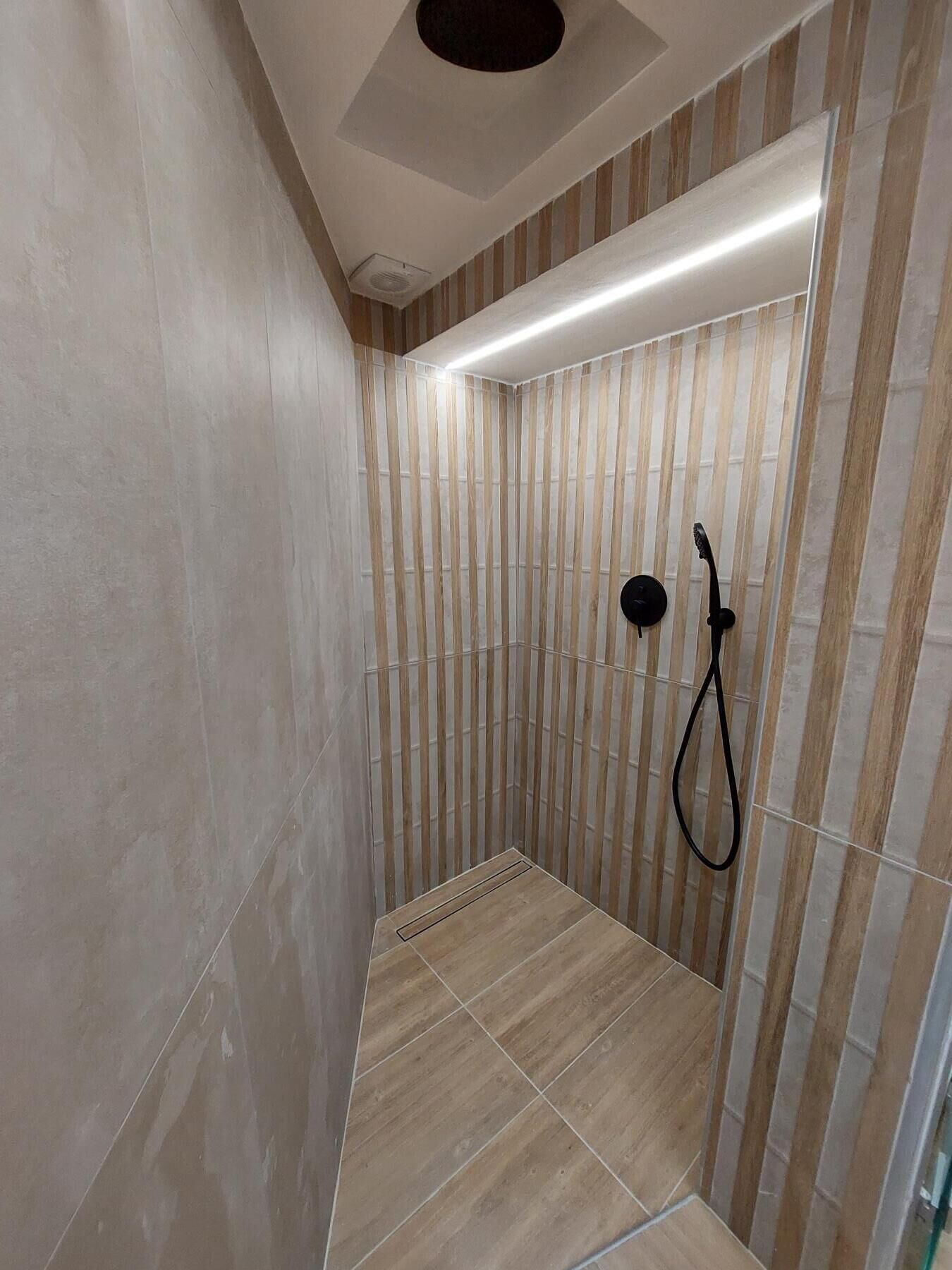Een moderne douche ruimte met gestreepte wandtegels en een inbouw plafondlamp.