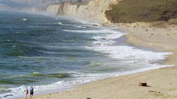A beach with waves crashing onto the shore, a sandy beach, and cliffs in the background. - Pescadero Creek Inn (Pescadero)