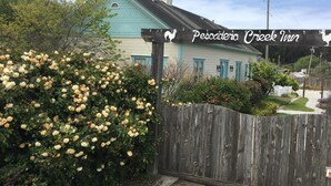 A wooden gate with a sign for Pescadero Creek Inn, a wooden fence, and a bush of yellow flowers. - Pescadero Creek Inn (Pescadero)