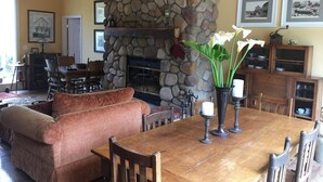 A cozy living room with a stone fireplace, a wooden dining table, and comfortable seating. - Pescadero Creek Inn (Pescadero)