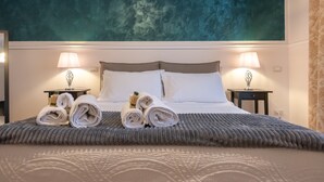 Una cama bien tendida con toallas enrolladas y dos lámparas de noche, un techo texturizado y una cortina con estampado floral.