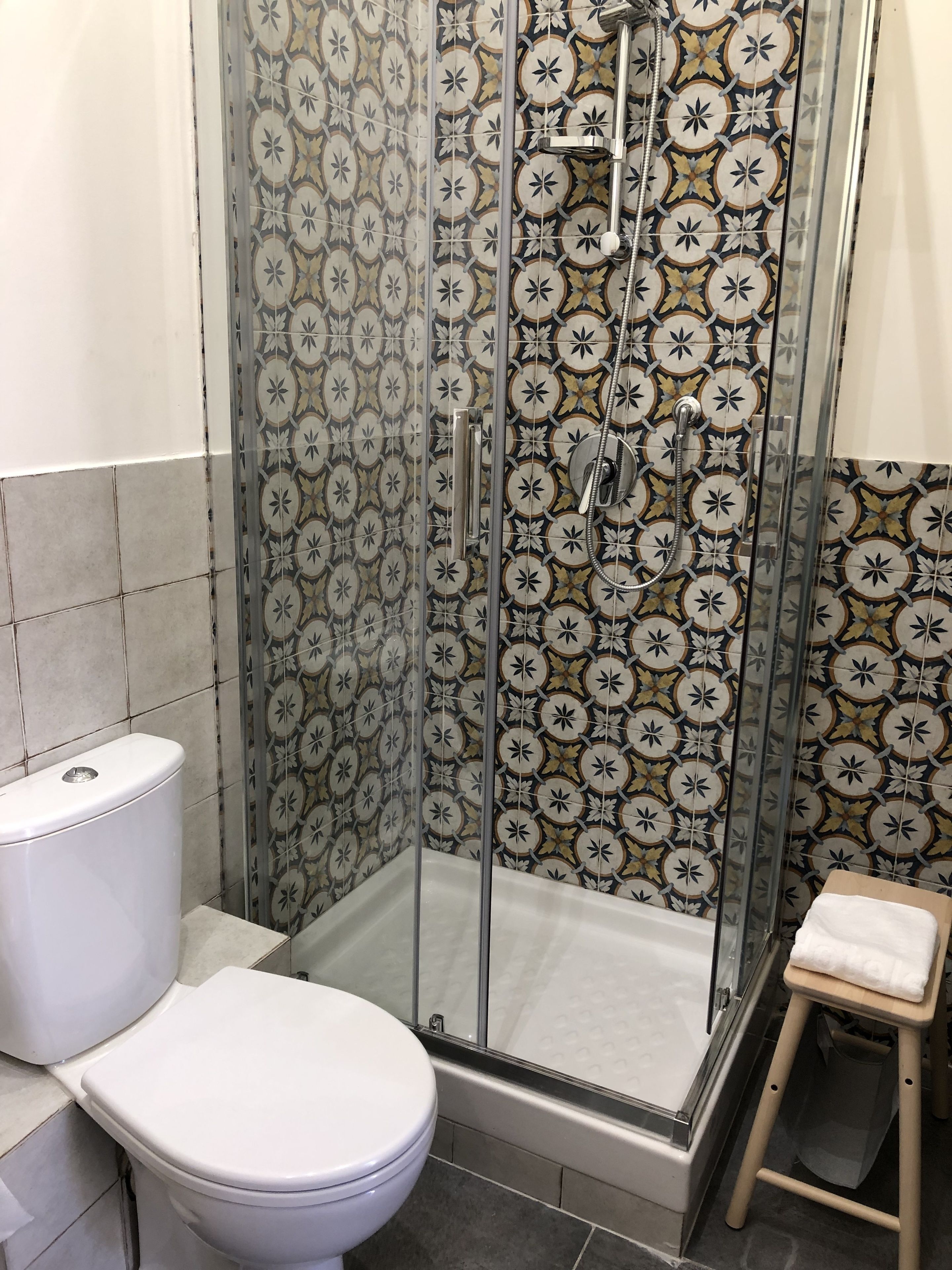 A bathroom with a shower enclosure, toilet, and a small stool.