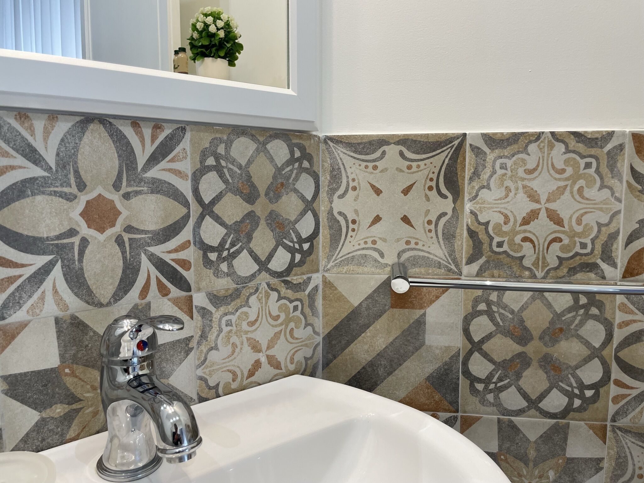 Un baño con lavamanos blanco, grifo cromado y azulejos decorativos en varios patrones y colores.