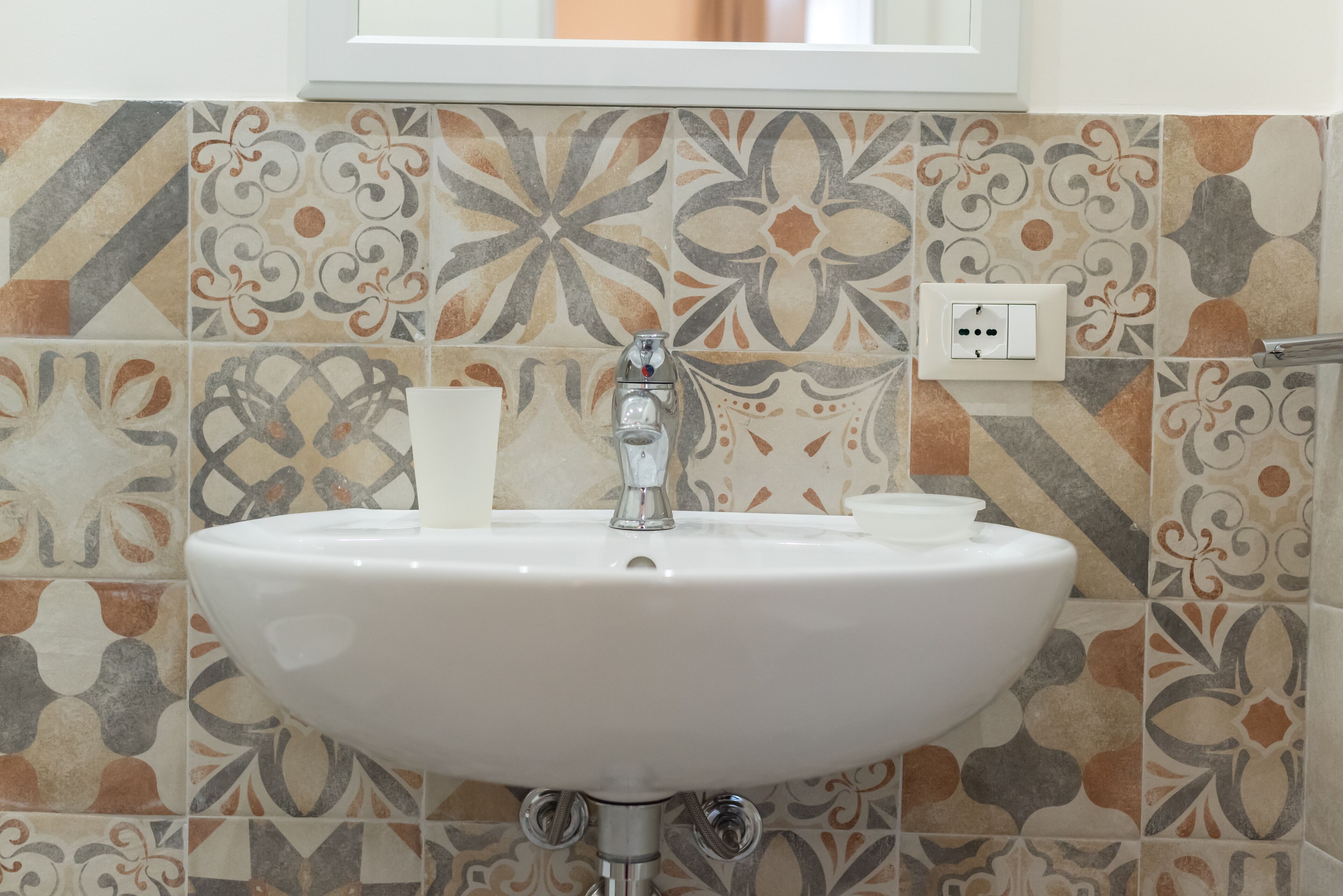 A bathroom with a white sink, a faucet, and a decorative tile backsplash.