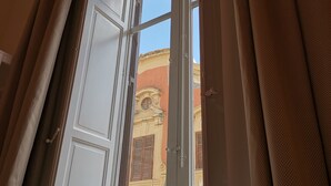 Una ventana abierta con cortinas, mostrando un edificio con fachada amarilla y un ventanal decorativo.