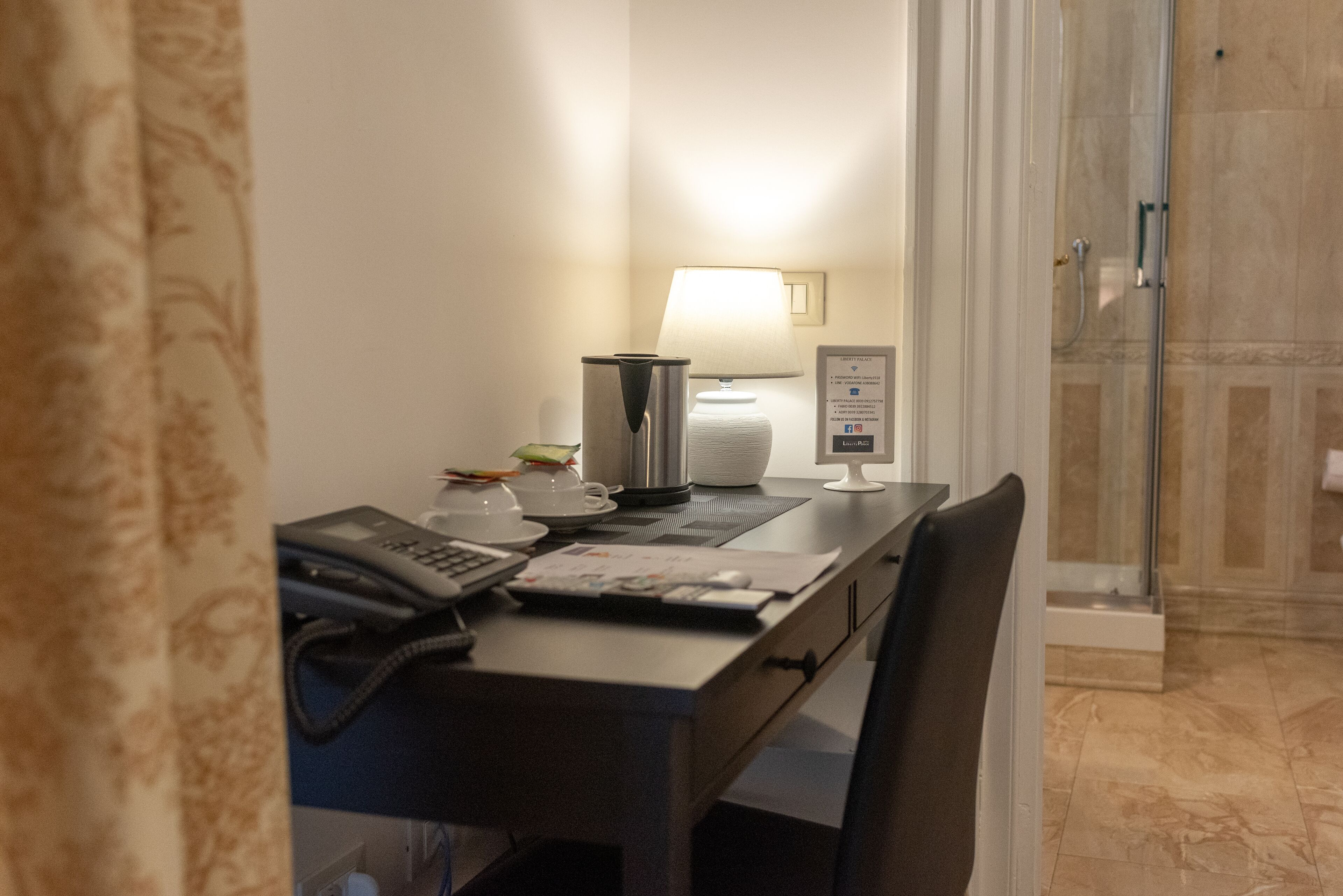A hotel room with a desk, a telephone, a lamp, a coffee maker, and a shower area.
