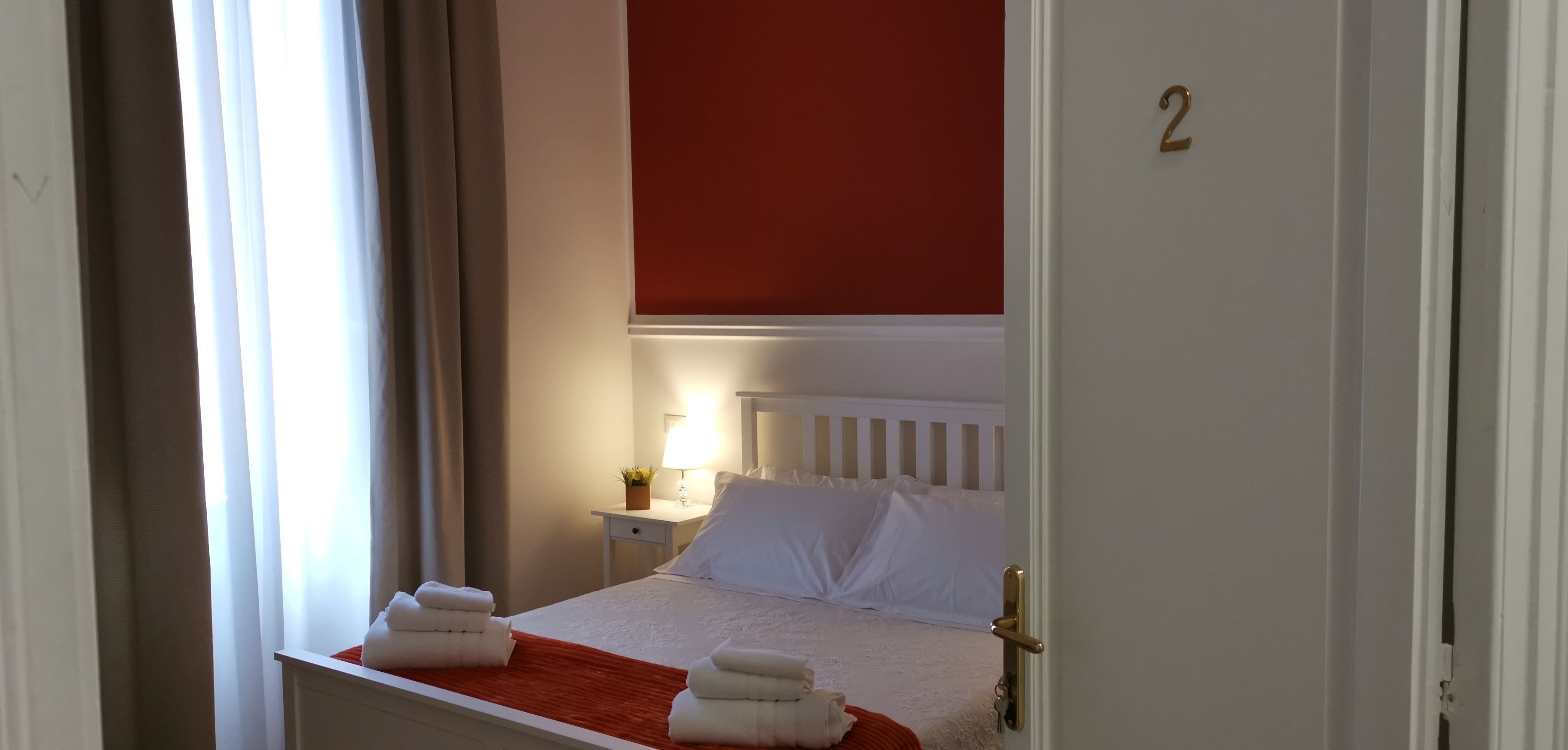 A hotel room with a bed, a nightstand, a lamp, and a door with a number.