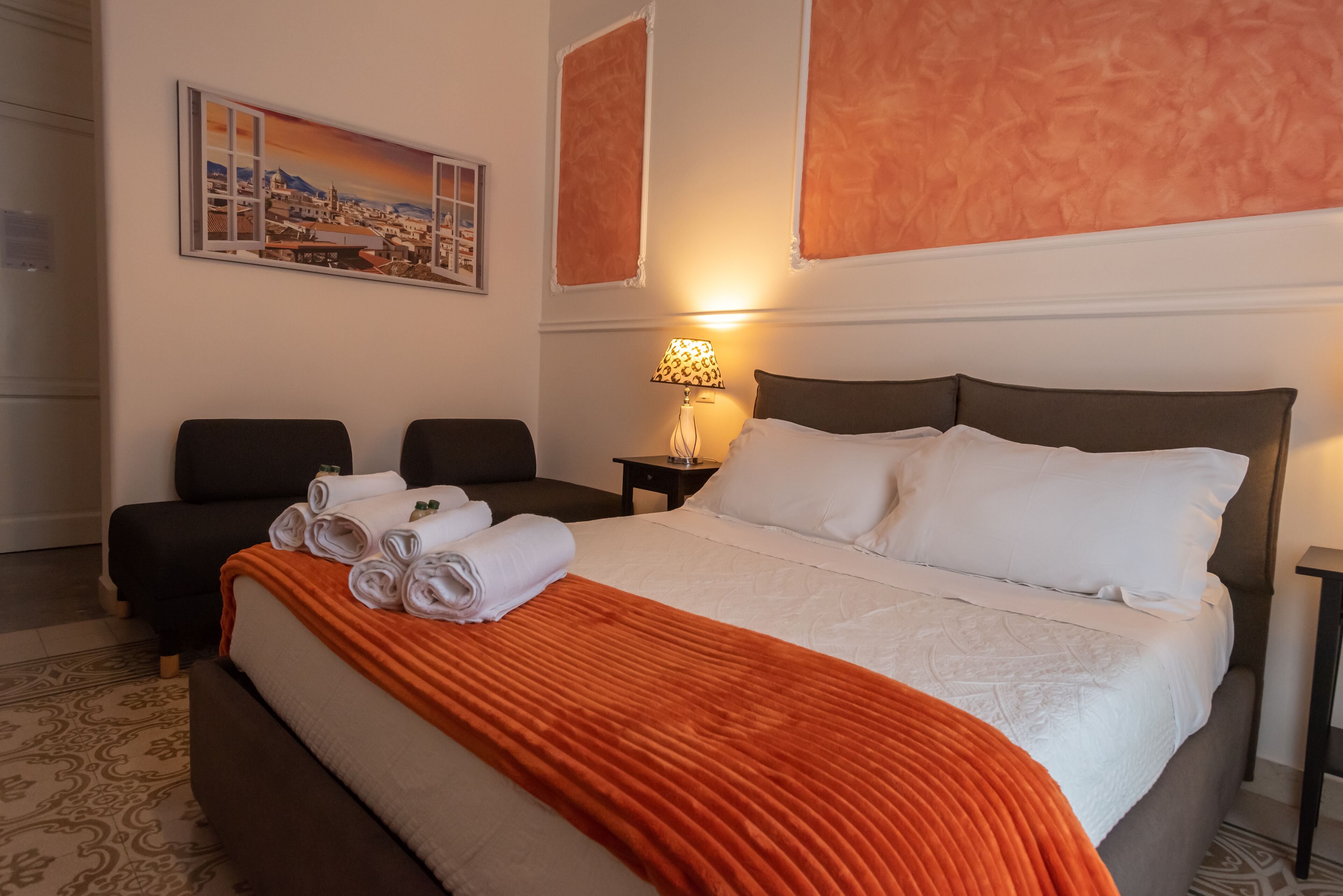 A hotel room with a large bed, a desk, two chairs, and a painting on the wall.