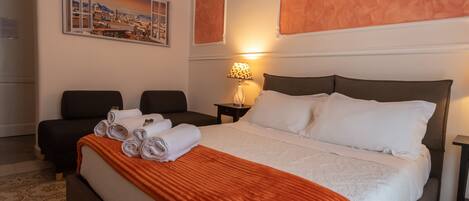 A hotel room with a large bed, a desk, two chairs, and a painting on the wall.