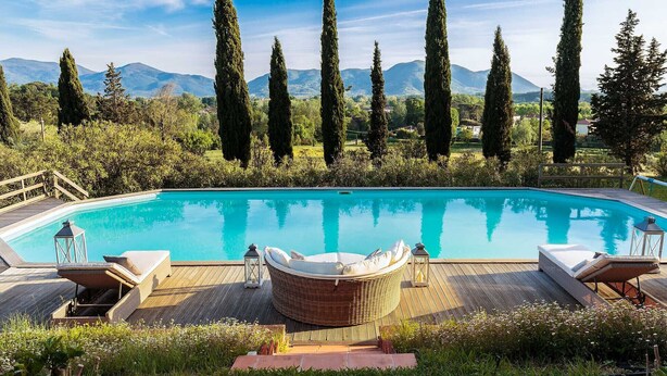 A swimming pool with a wooden deck, lounge chairs, and a wicker chair. - VILLA D'AMICO, charming indulgence overlooking Lucca Town Centre (Lucca)