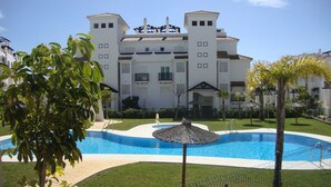 A large building with a swimming pool, surrounded by greenery and palm trees. - Residencial Duquesa 2049  Manilva Beach (Manilva)