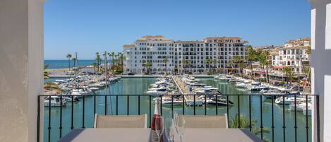 A balcony with a view of a marina, boats, and a hotel building in the background.