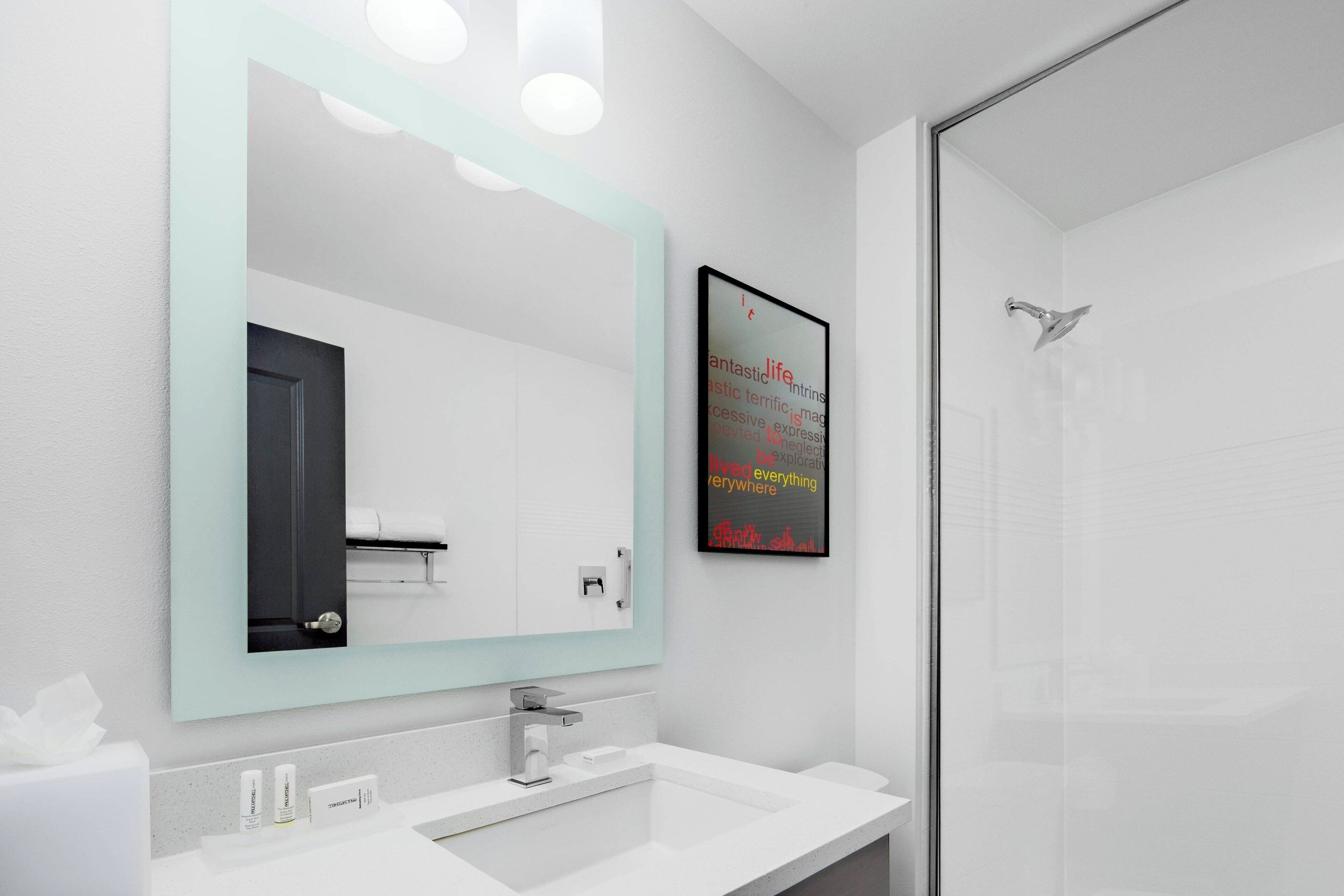 Un bagno moderno con uno specchio grande, una doccia e una citazione motivazionale incorniciata al muro.
