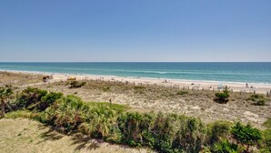 Een strand met een hek, mensen op het strand en een heldere lucht.
