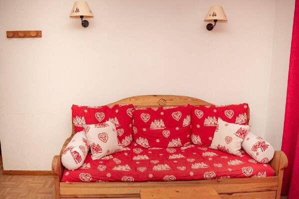 Un sofá de madera con cojines estampados en rojo y blanco, dos lámparas fijadas a la pared y un panel de madera en la pared.