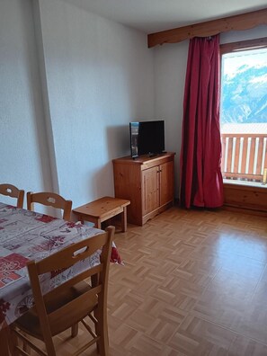 Una habitación con una mesa y sillas de madera, un televisor sobre un mueble de madera y una ventana que ofrece vistas a las montañas.