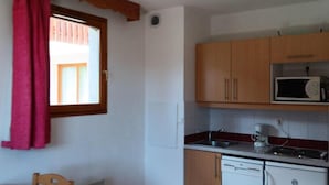 Una piccola cucina con mobili in legno, un forno a microonde, una macchina da caffè e un tavolo da pranzo con tovaglia rossa.