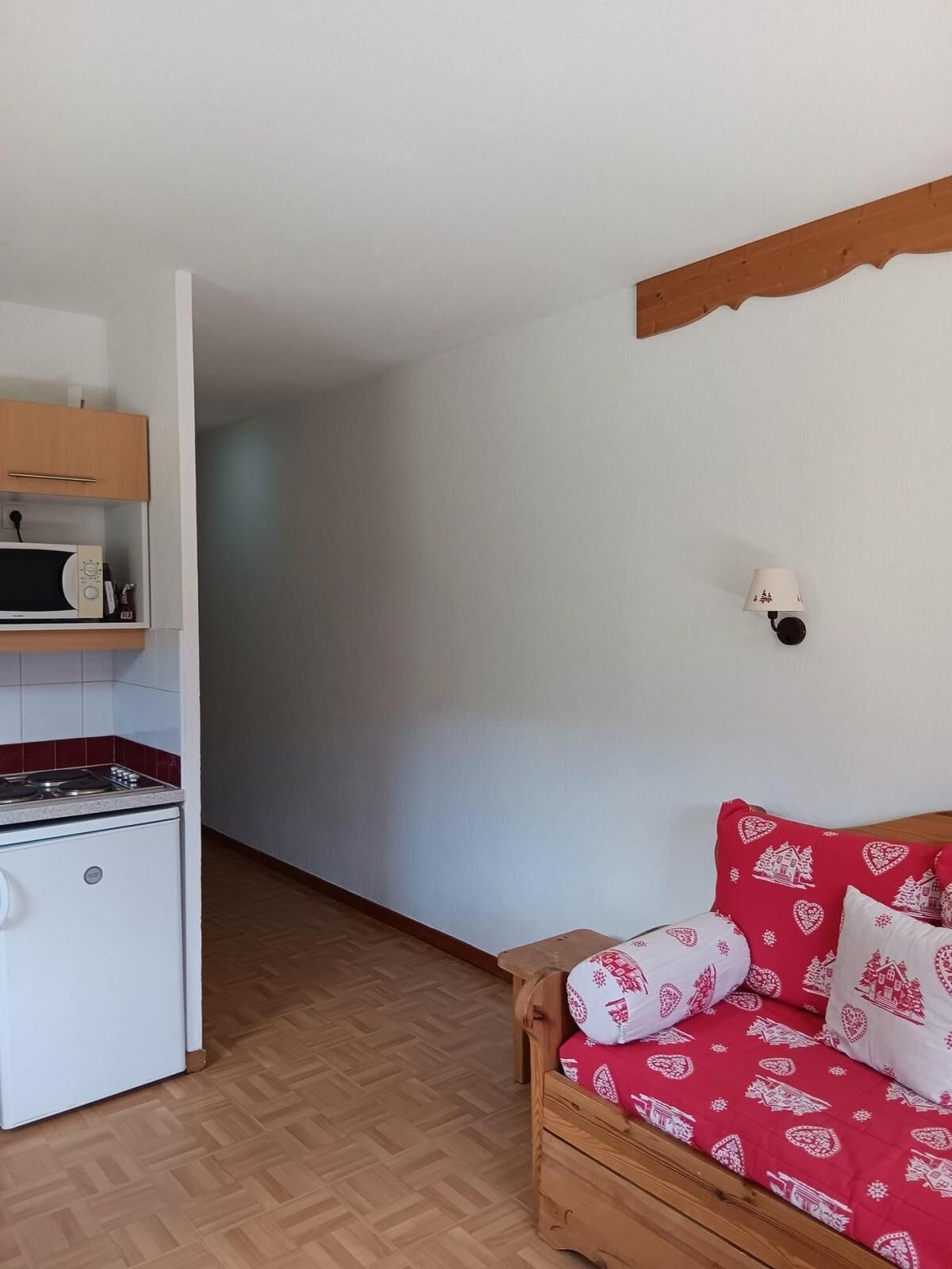 A compact kitchen with a microwave, stove, and wooden cabinets. A wooden bench with red and white patterned cushions is against the wall.