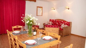 A dining area with a wooden table set for four, a vase of flowers, and a red sofa in the background. - Wifi, 2nd floor, swimming pool, balcony, parking, tv, ski locker, 60m², Puy-Saint-Vincent (Puy-Saint-Vincent)