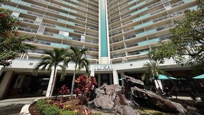 A high-rise hotel with multiple balconies, a central vertical feature, and a landscaped area with rocks and plants. - Lagoon & Ocean View Ilikai Studio 1042  – Walk to Waikiki Beach | Sleeps 4 | Renovated Condo (Waikiki)