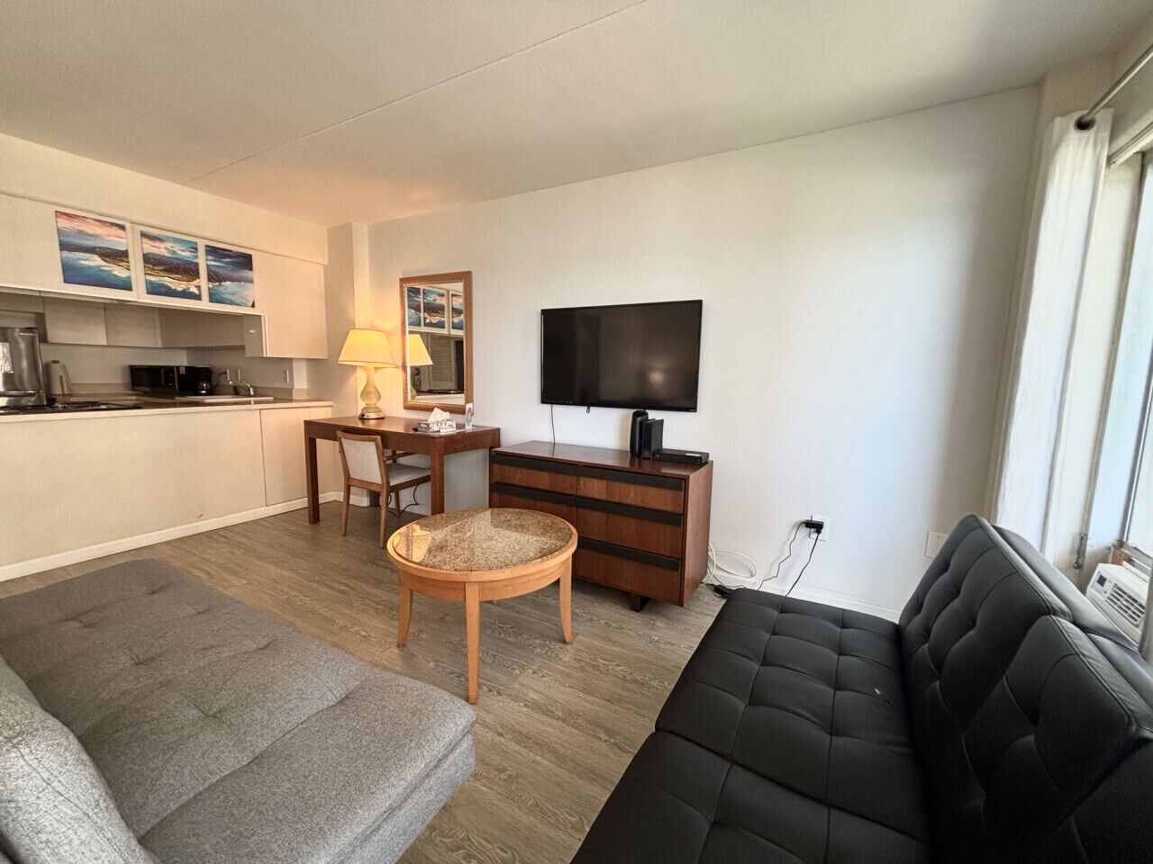Een knus woongedeelte met een bank, een eettafel met stoelen, een kleine keuken en een flatscreen televisie aan de muur.