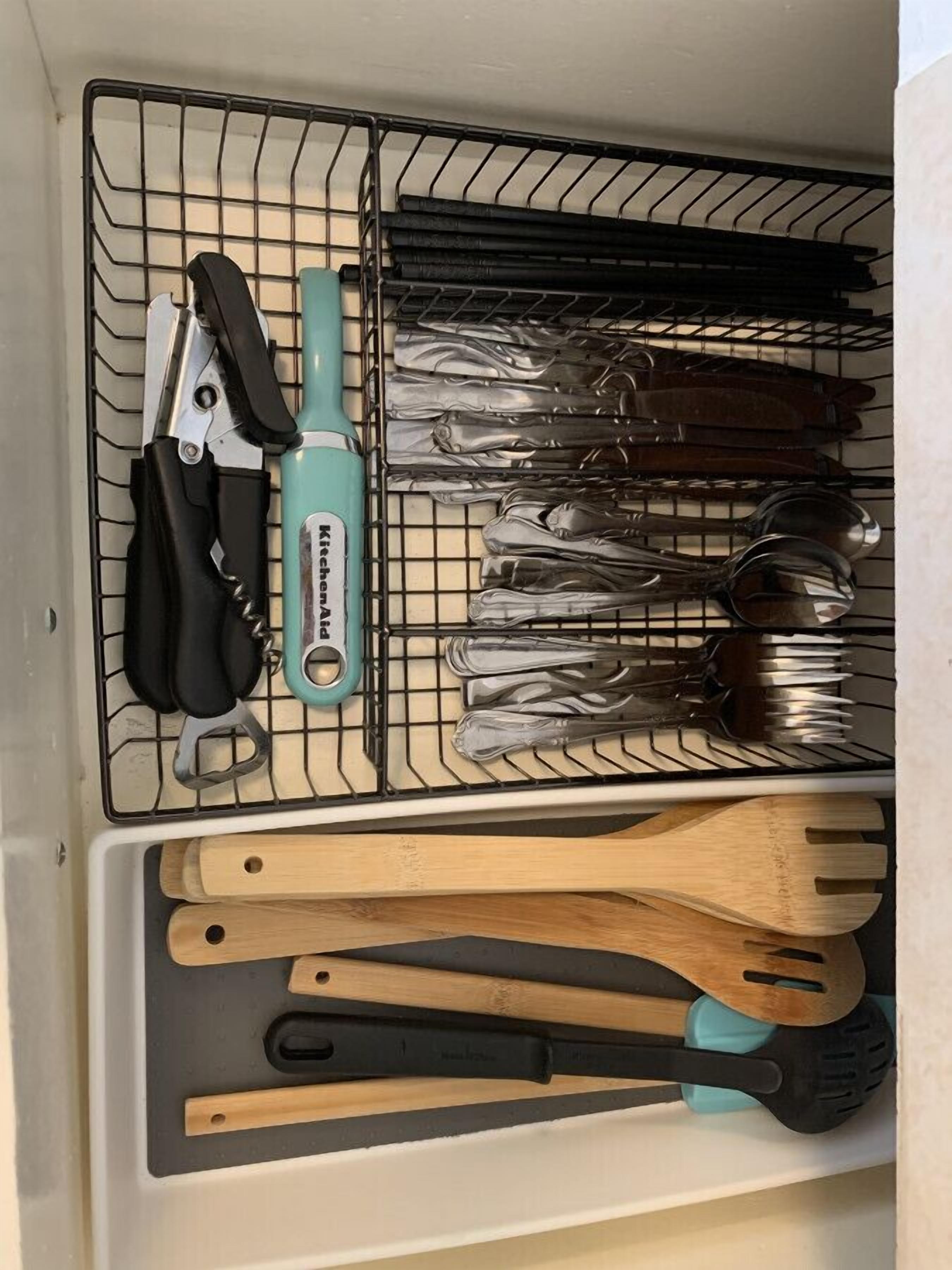 Un cajón de cocina con un escurridor que contiene varios utensilios de cocina, como cuchillos, cucharas y un rallador.