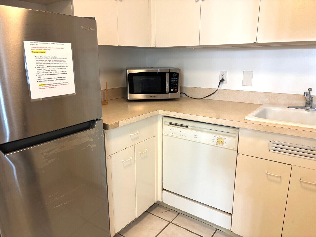 Eine kompakte Küche mit Edelstahl-Kühlschrank, Mikrowelle und Geschirrspüler.