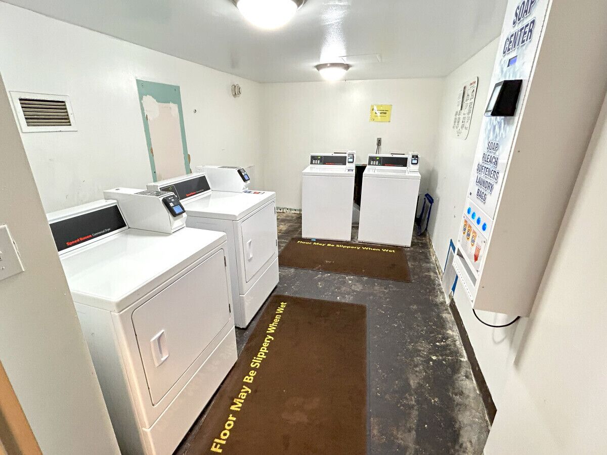 A laundry room with two washing machines, a dryer, and a soap dispenser on the wall.