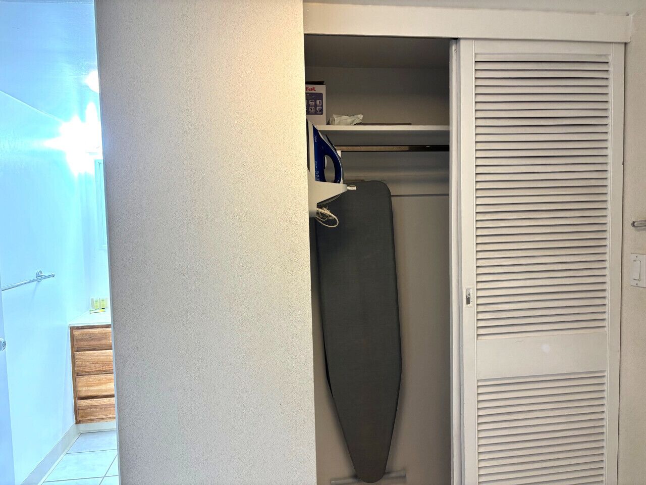 Ein Schrank mit Kleiderstange, Ablagefläche und einer Tür mit Lamellen.