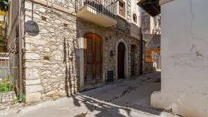 Una estrecha calle adoquinada con edificios de piedra, puertas de madera y una reja metálica.