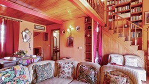 Una sala de estar acogedora con un sofá a cuadros, una escalera de madera y una estantería llena de libros.