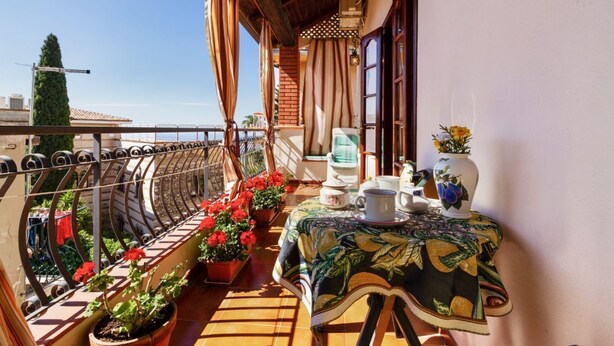 Un balcón con plantas en macetas, una mesa con mantel y vista al mar.