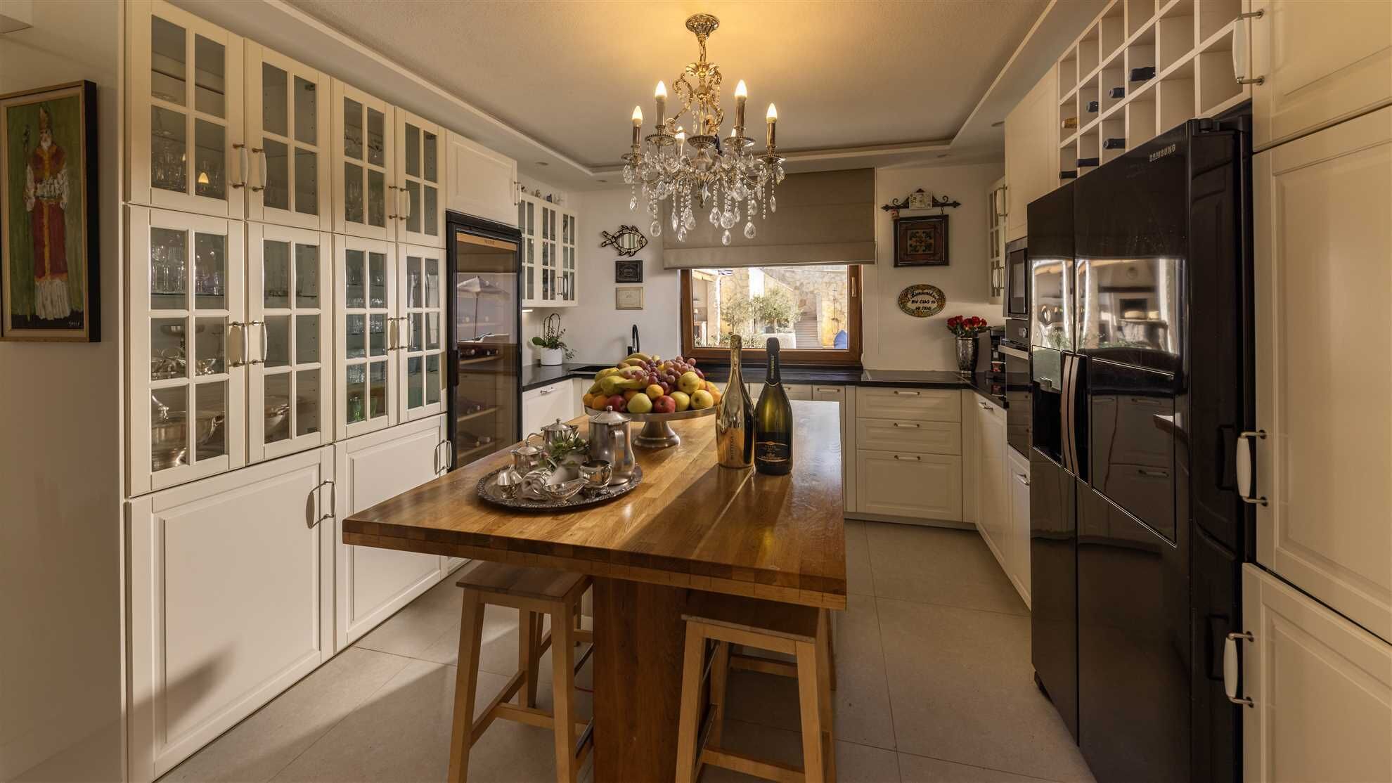 A kitchen with white cabinetry, a wooden island with stools, a black refrigerator, and a chandelier.