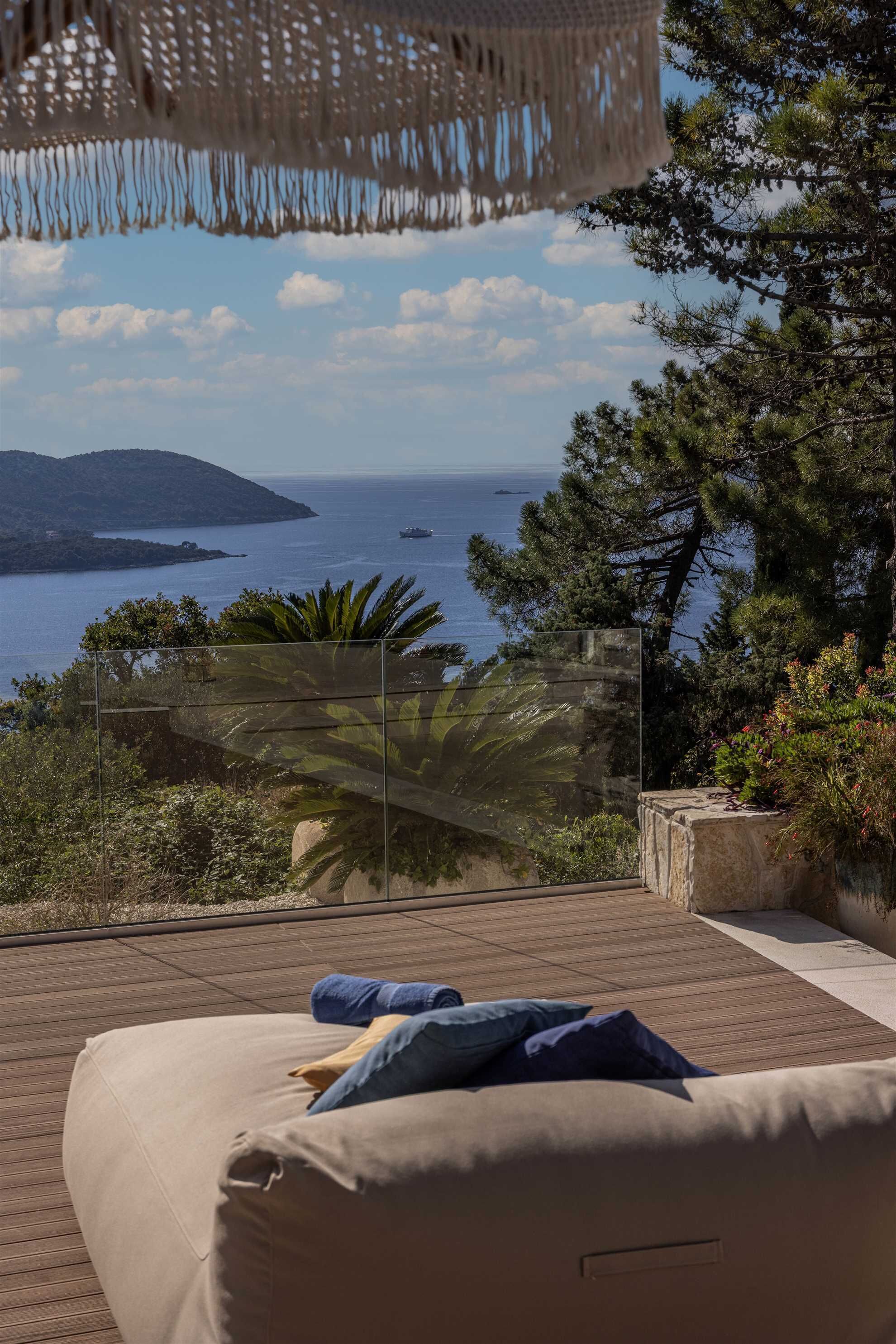 A balcony with a view of the sea, a glass partition, and a cushioned seating area.
