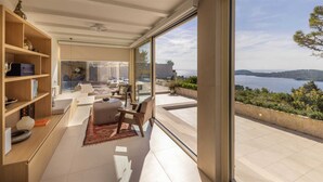 A modern living room with a large glass door leading to a balcony with a scenic view of the sea.