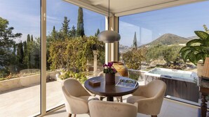 A modern outdoor seating area with a table, chairs, and a hot tub, overlooking a scenic landscape with trees and mountains.