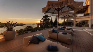 A rooftop terrace with a view of the sea and mountains, featuring outdoor seating and a decorative umbrella.
