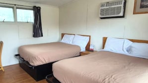Une chambre d’hôtel avec deux lits, un plancher en bois, un appareil de climatisation et une fenêtre avec des rideaux.