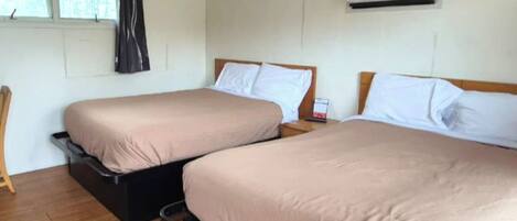 Habitación de hotel con dos camas, piso de madera, equipo de aire acondicionado y ventana con cortinas.