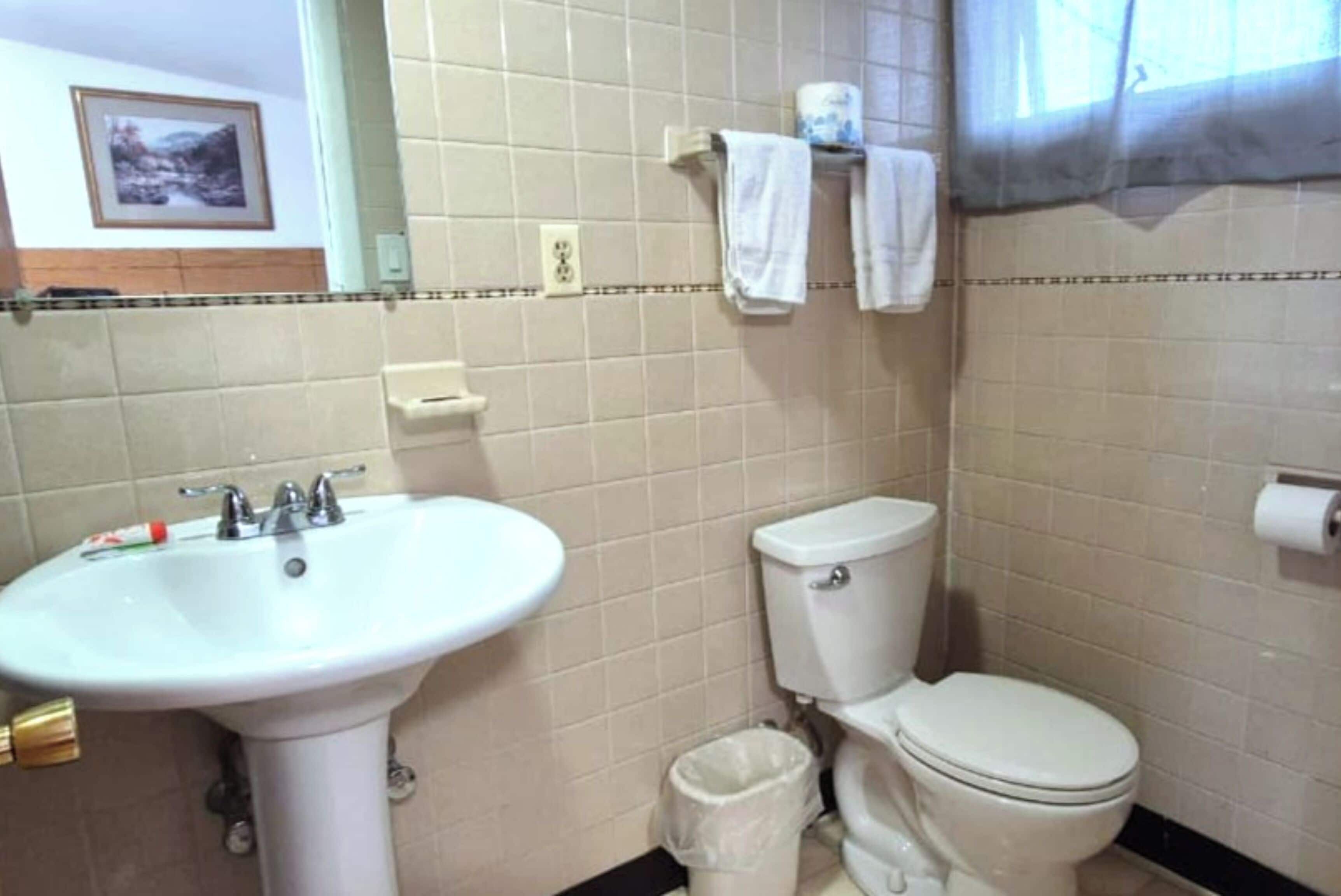 Un baño con lavamanos blanco, inodoro y cubo de basura.