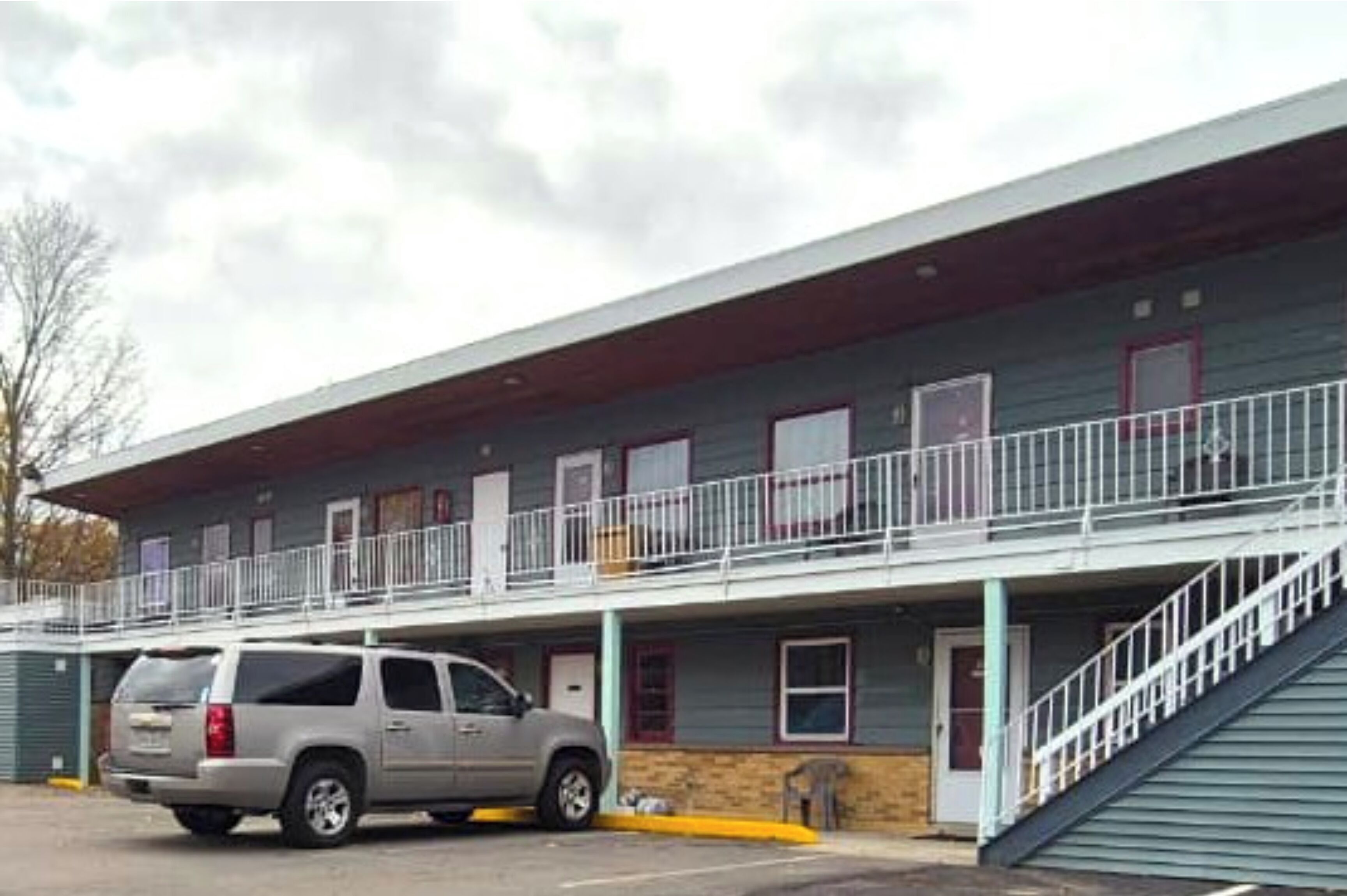 Um motel com estrutura em dois andares, área de estacionamento coberta e escadaria que leva ao nível superior.